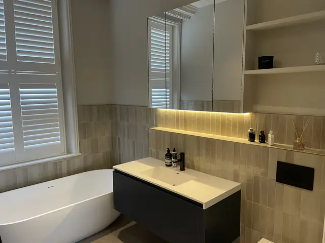 Modern bathroom with freestanding white bathtub, dark vanity, and large backlit mirror cabinet.