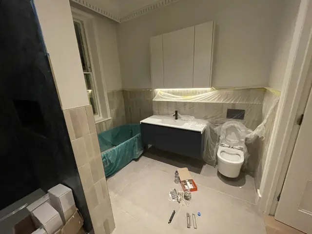 Bathroom in progress with dark blue vanity, wall-hung toilet, and construction materials.