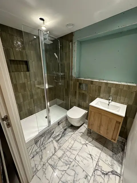 Modern bathroom with marble flooring, walk-in shower, wall-hung toilet, and wooden vanity unit.