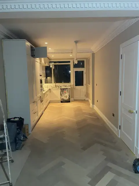 Full view of a cream kitchen with herringbone flooring during finishing stages.