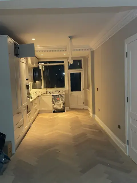 Long kitchen view with cream cabinets and herringbone wood flooring.