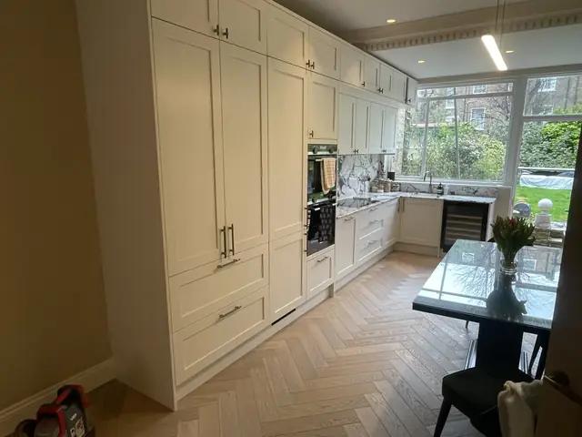 Elegant cream kitchen with full-height cabinetry, marble surfaces, herringbone flooring, and dining area.