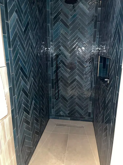 Luxurious dark blue herringbone tiled shower enclosure with black modern fittings.