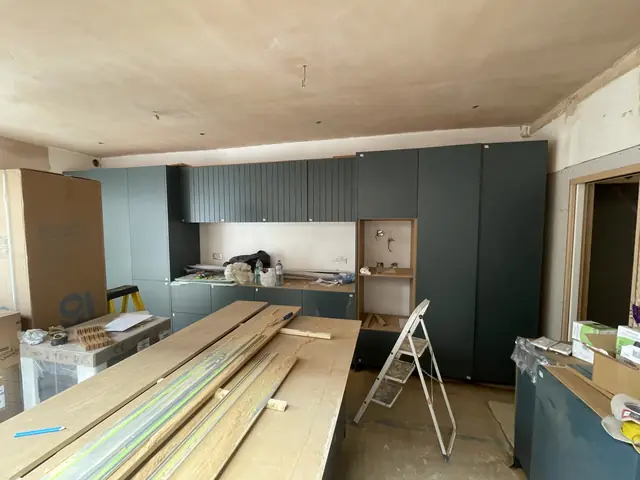 Construction view of dark green kitchen cabinetry installation in progress.