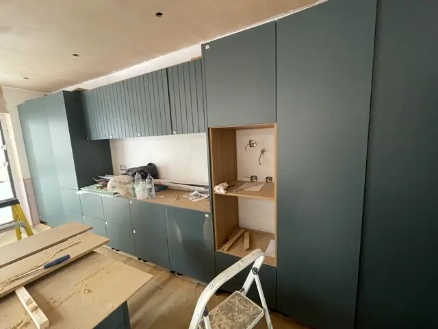 Dark green kitchen cabinetry during installation with visible construction elements.