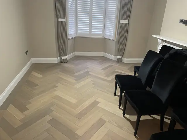 Dining area with black velvet chairs and light herringbone wood flooring next to a bay window.