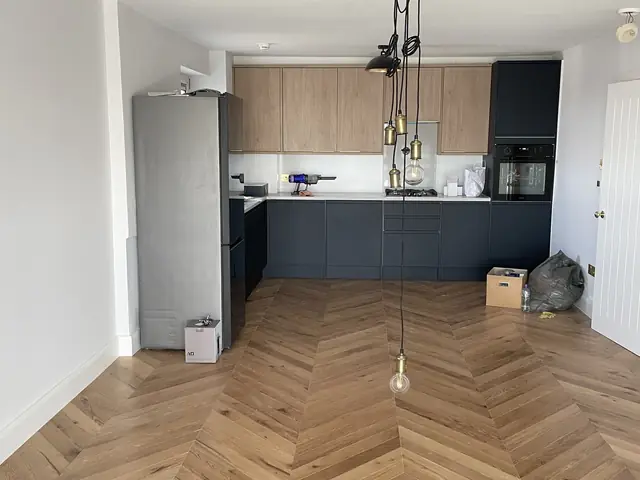 Modern empty kitchen with light wood and dark grey cabinetry on herringbone wood flooring.