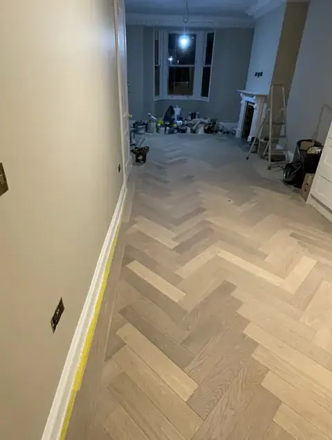 Hallway with light herringbone flooring leading to a room under renovation.