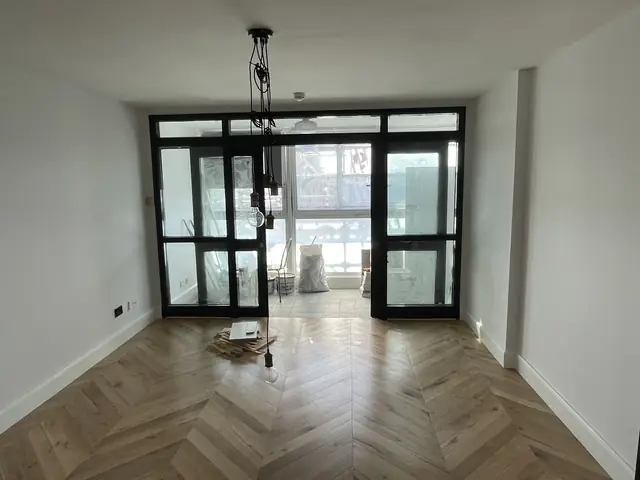 Spacious empty room with light herringbone wood flooring and large black bifold doors.