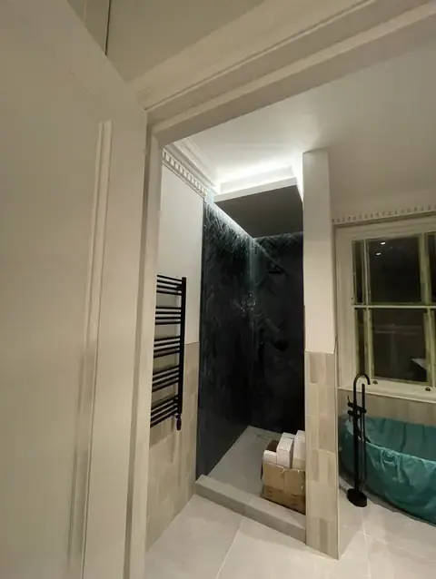 Dark herringbone tiled walk-in shower next to a bathroom with bathtub.