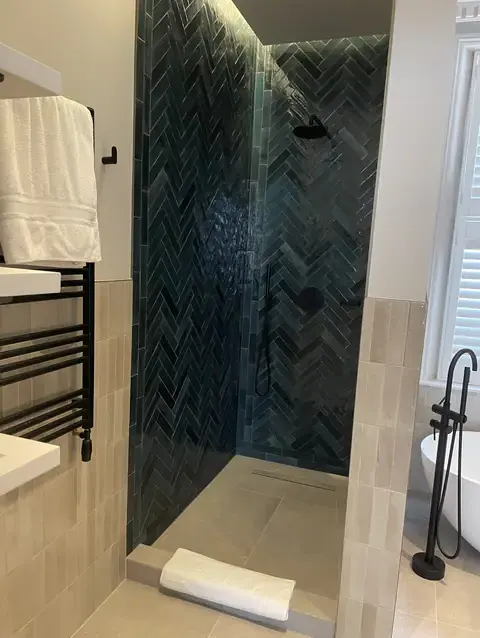 Luxurious dark herringbone tiled walk-in shower with black modern fittings.