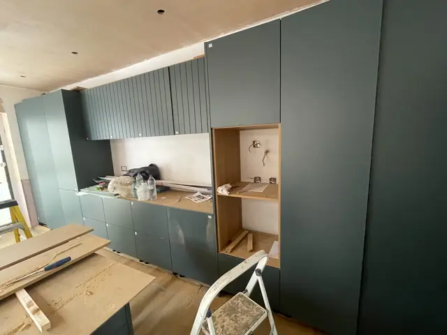 Kitchen in progress with dark green cabinetry and construction materials on site.