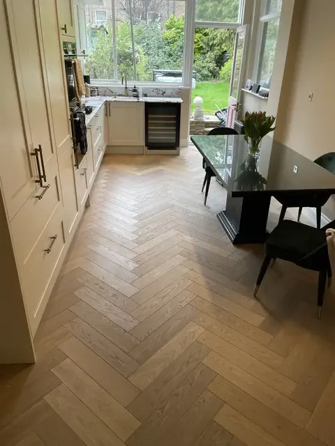 Bright kitchen and dining area with cream cabinetry, marble surfaces, and herringbone flooring overlooking the garden.