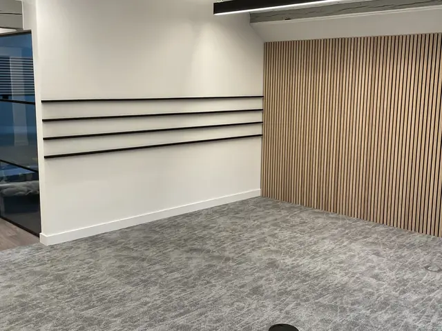 Modern room with grey carpet, wooden slat accent wall, and minimalist design.