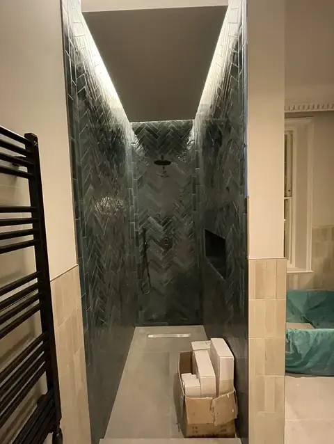Narrow dark herringbone tiled walk-in shower enclosure.