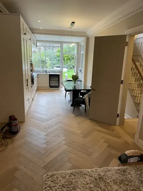 Open-plan kitchen, dining, and living area with light herringbone flooring and cream cabinetry.
