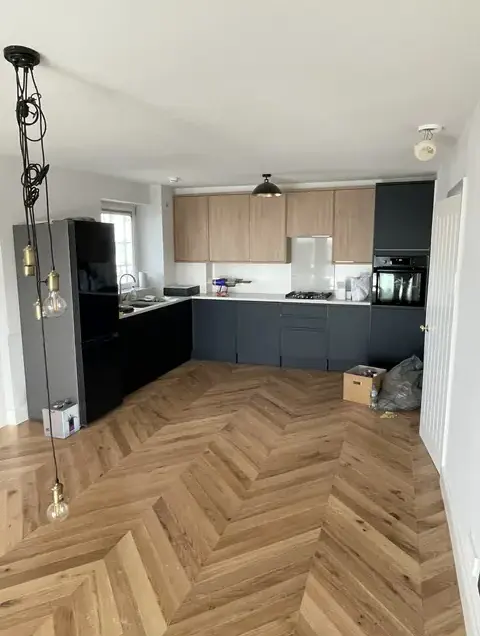 Modern open-plan kitchen with dark grey and wood cabinetry on light herringbone wood flooring.
