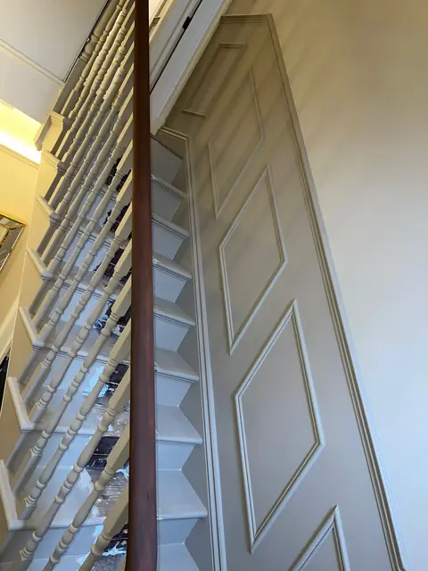 Traditional staircase with cream spindles and decorative cream paneling on the wall.
