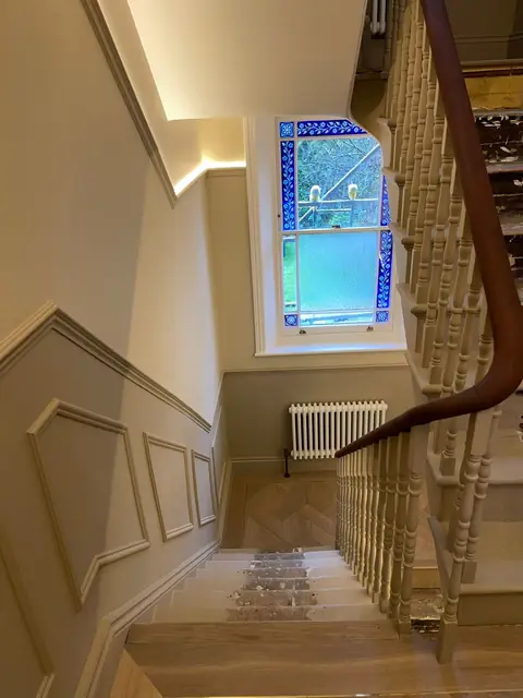 Elegant staircase with cream paneling, wooden steps, and a beautiful blue stained-glass window at the landing.