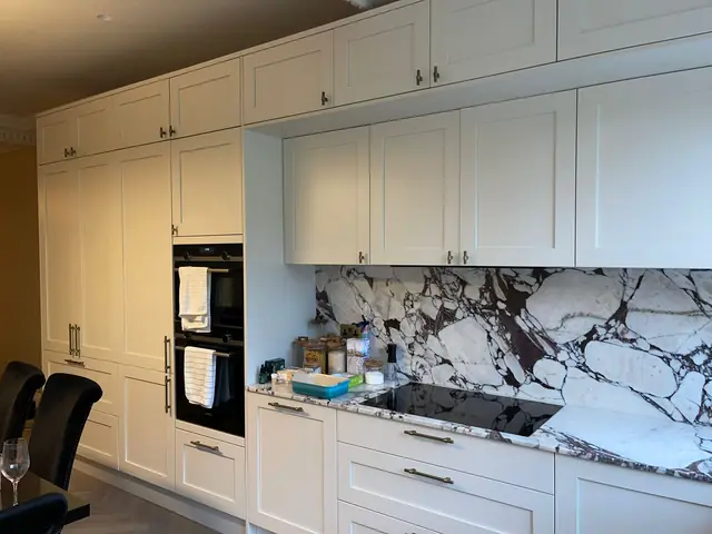 Bright white modern kitchen with extensive cabinetry, built-in appliances, and dramatic marble-patterned worktops and splashback.